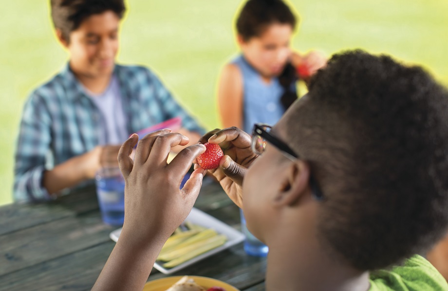 Kid holding raspberry while sitting outside at picnic table