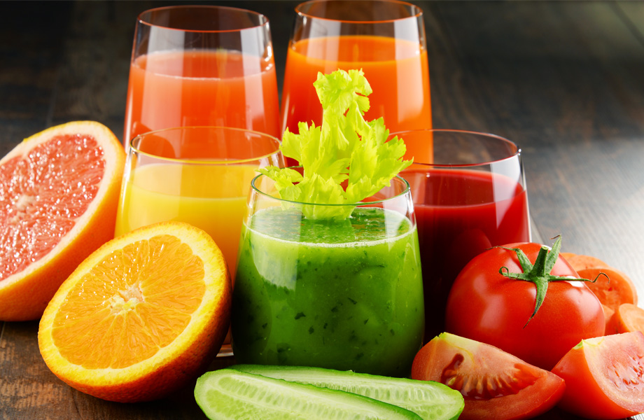 Different vegetable and fruit juices in glasses with oranges, tomatoes, limes, and grapefruits