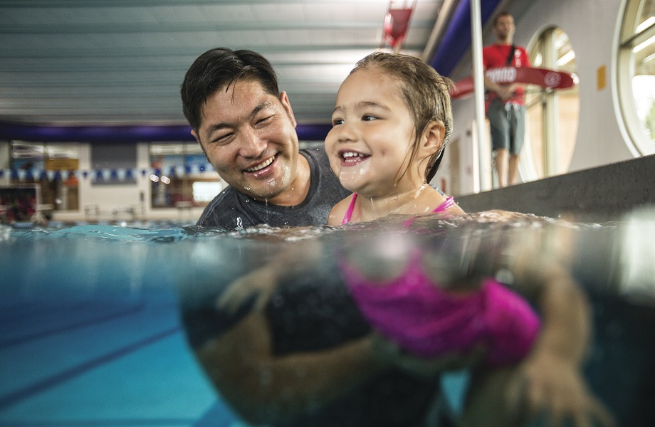 Father and daughter swimming together in indoor pool
