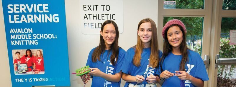 Three girls showing off their knitting projects during the YMCA After School Zone at Avalon Middle School in Orange County, Florida