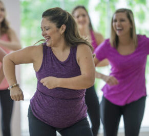 A group of women are working out at the gym and are taking an aerobic dance fitness class.