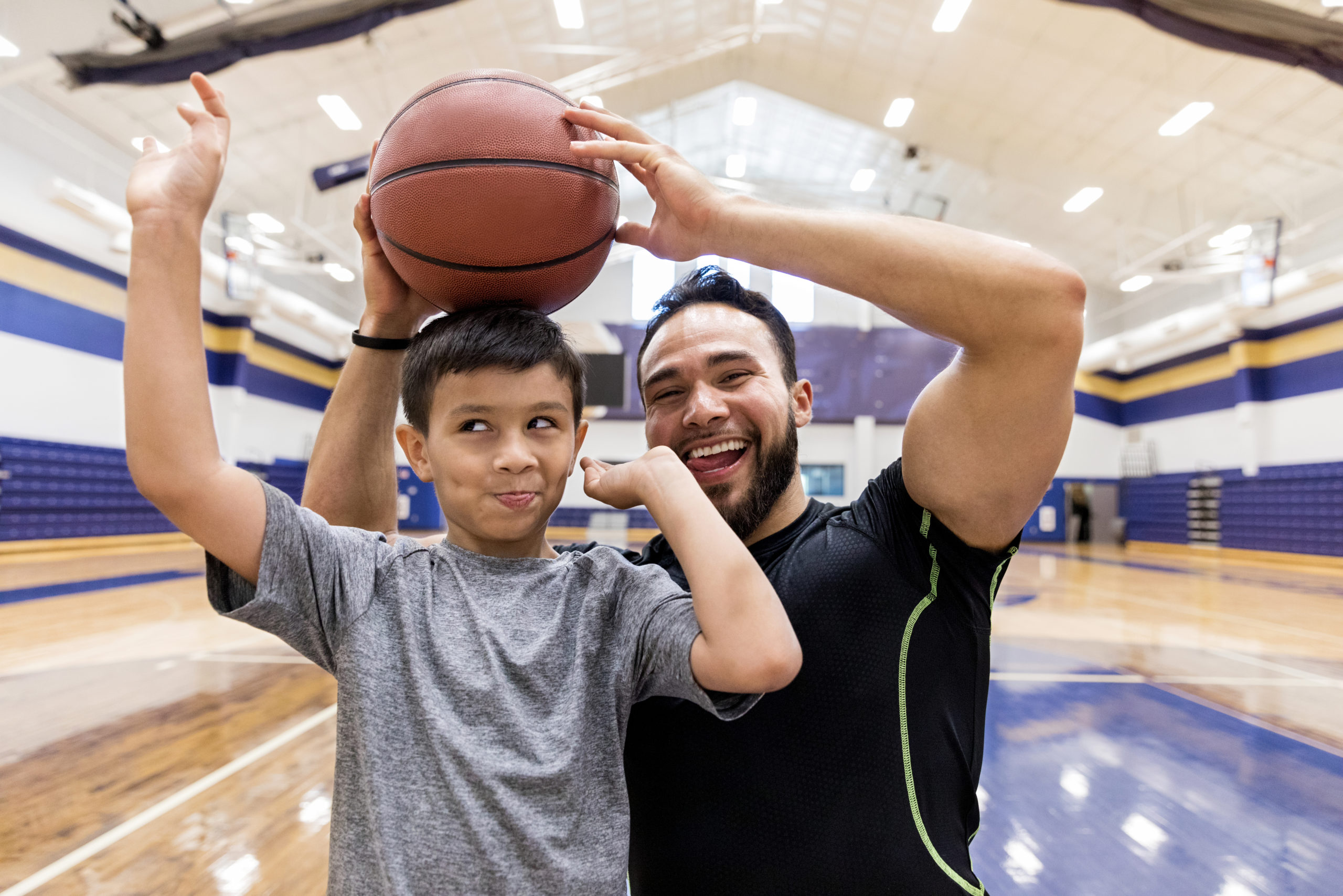 During a break from their basketball games, the mid adult father and his elementary age son goof off for the camera.