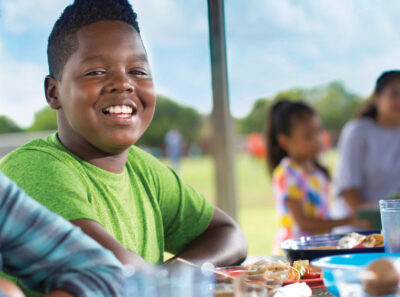 Boy sitting outside during summer camp wearing green t-shirt