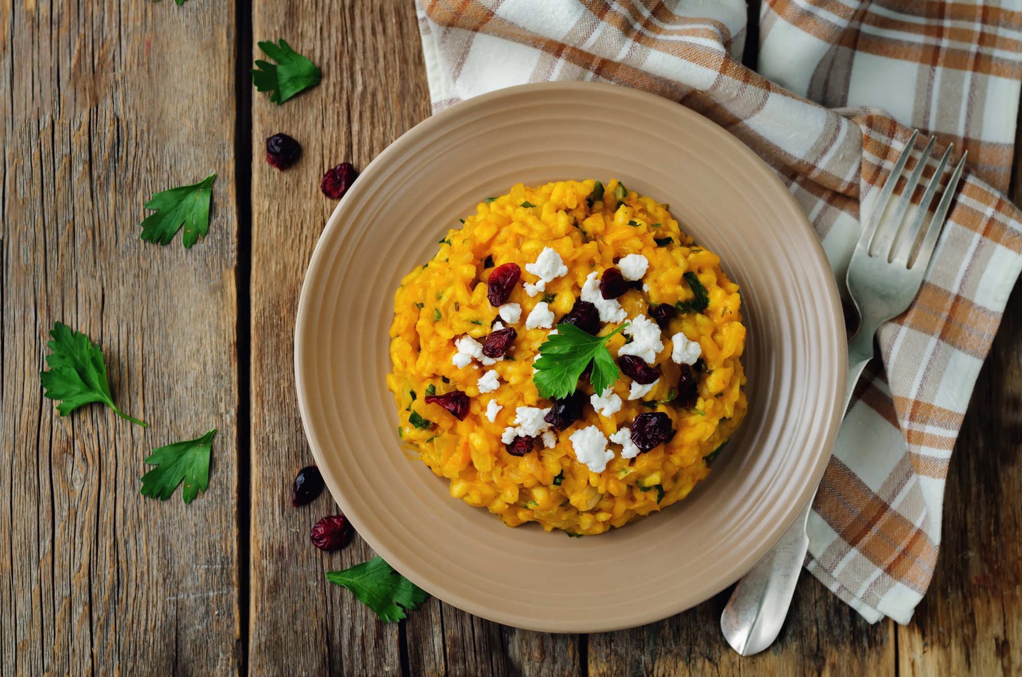 Pumpkin Goat Cheese Risotto in brown bowl on wooden table next to brown plaid tablecloth