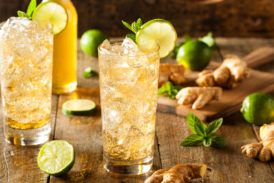 Three Ginger Lime Sparkling Waters in Glasses surrounded by limes and ginger on a wooden surface