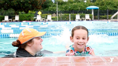 Girl in pool next to woman swim instructor similing as she learns to swim
