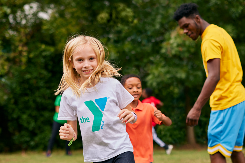 Young girl running in line outdoors wearing white t-shirt with green and blue Y logo on it
