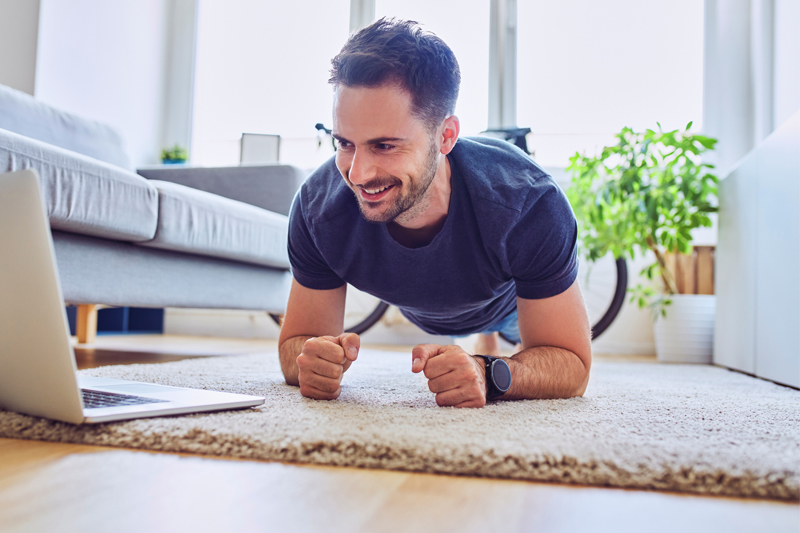 Man doing elbow plank while looking at a laptop in the living room on a rug