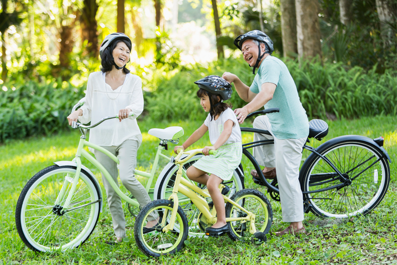 Two grandparents and a granddaughter on bicycles in the grass laughing together