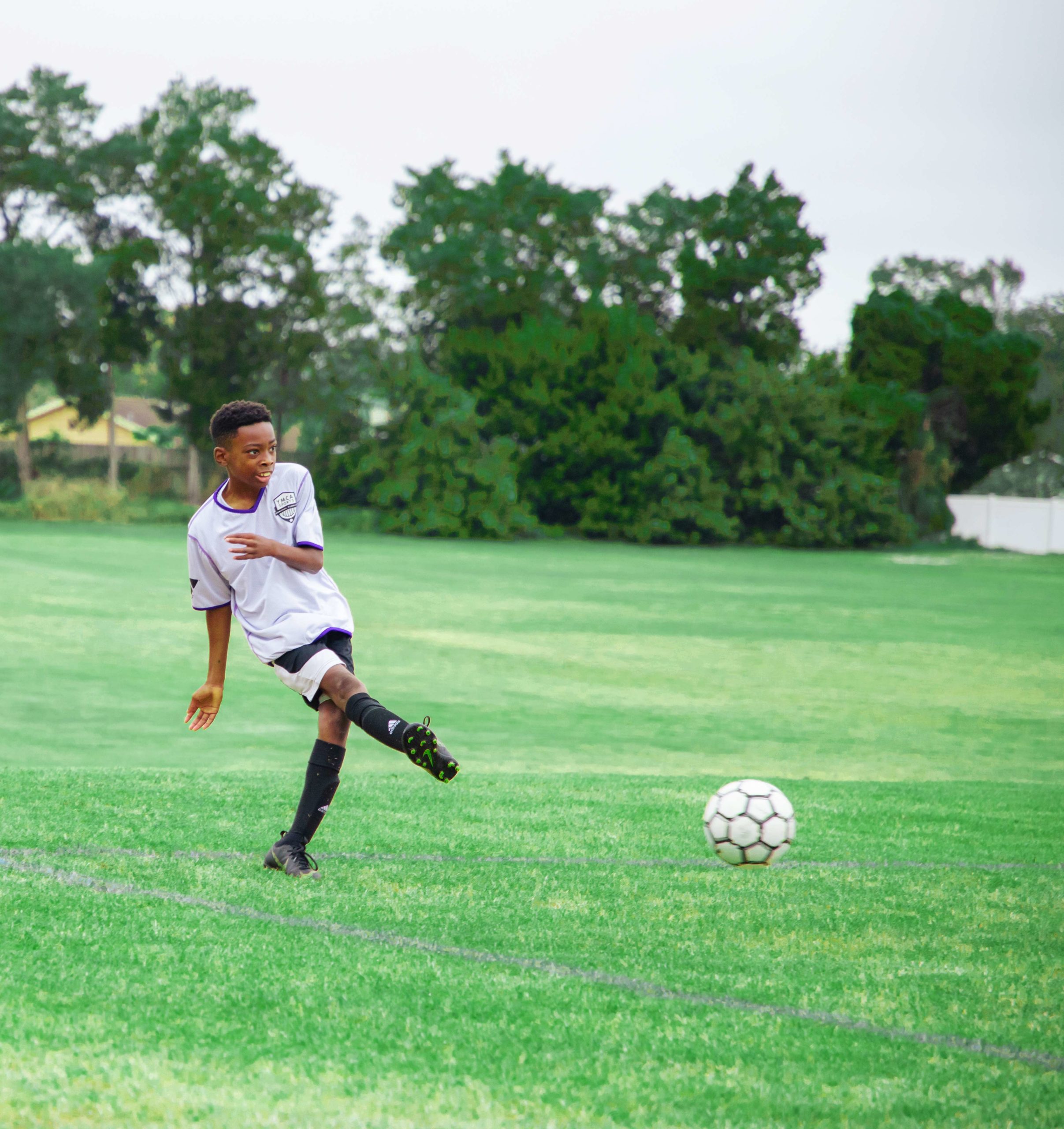 Photo of young by wearing gray Y Sports uniform while kicking a soccer ball on the soccer field