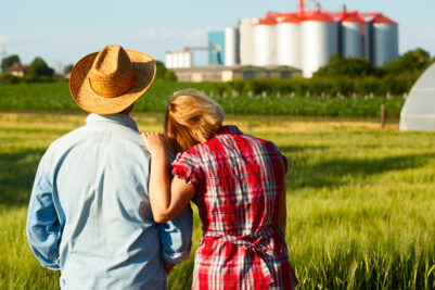 Farmer and his wife embracing while looking over the hills of their farm and the silos in the landscape