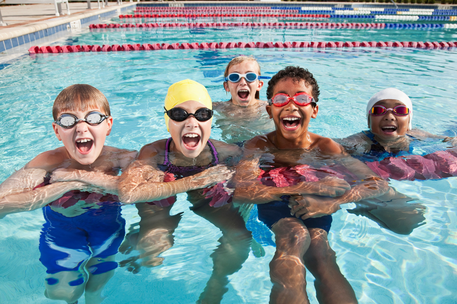 Multicultural group of children on a swim team wearing swimming hats and goggles, smiling, and celebrating a win