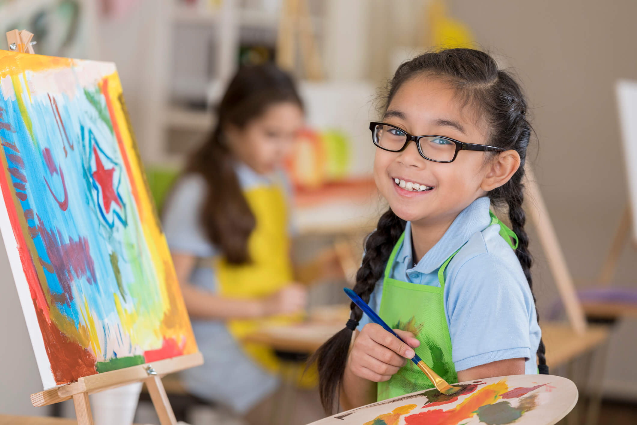 Girl smiling while holding paintbrush and looking at canvas