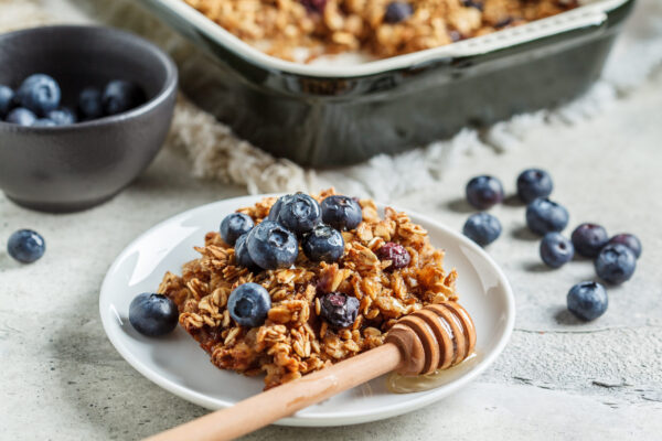 A photo of oatmeal with blueberries on top with a spoon of honey next to it