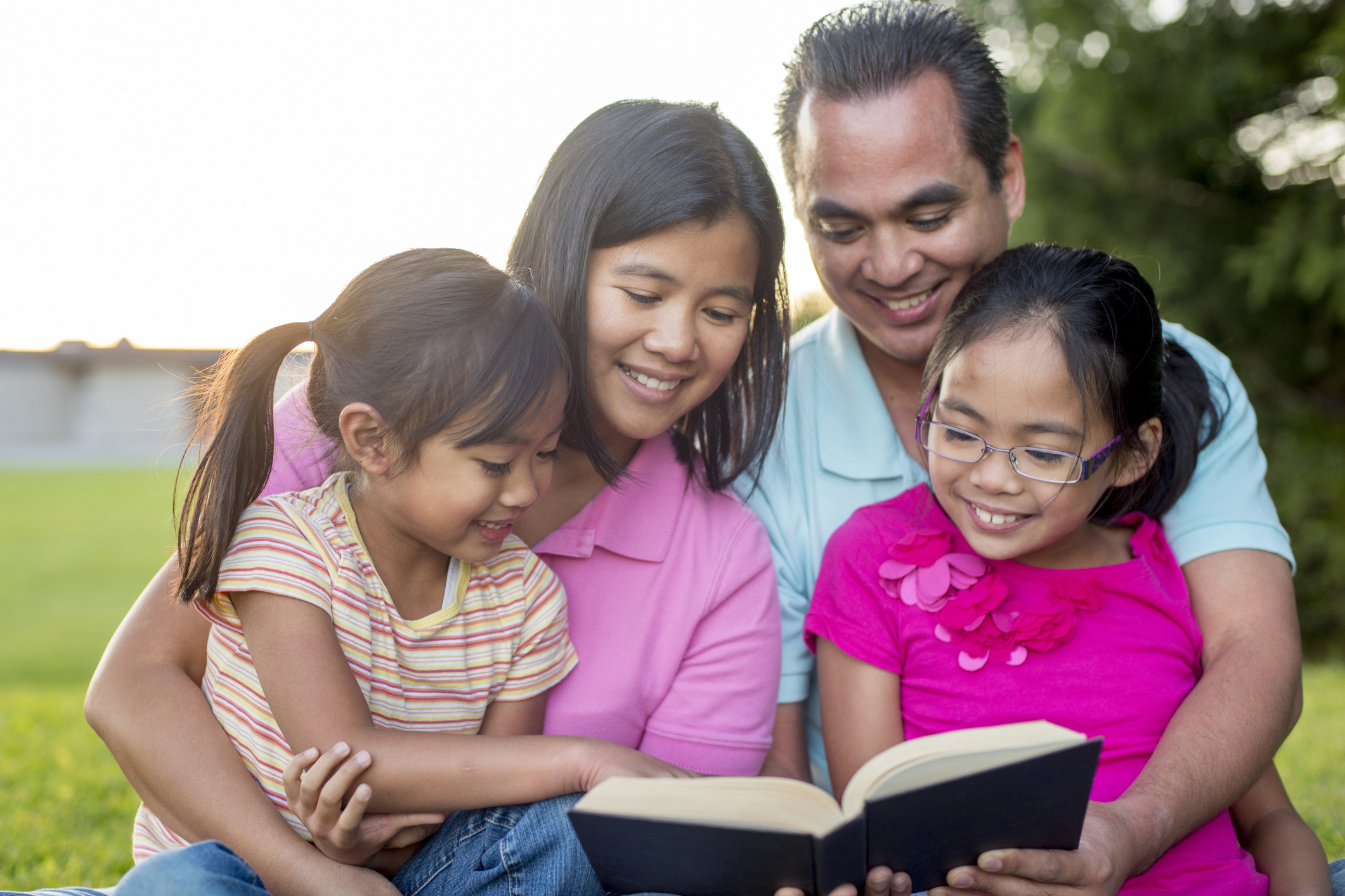 Family of four reading the Bible in the grass and smiling