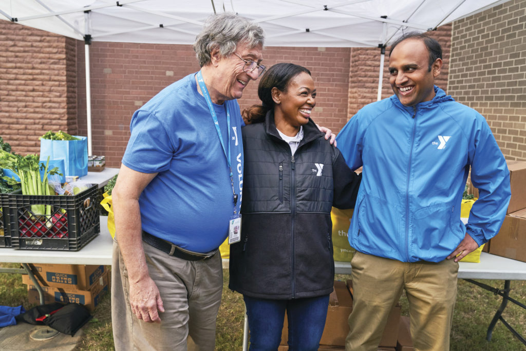 Group of YMCA volunteers laughing while standing outdoors during a food drive
