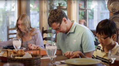 Image of Pastor Chad Garmon praying at a dinner table with his children praying beside him