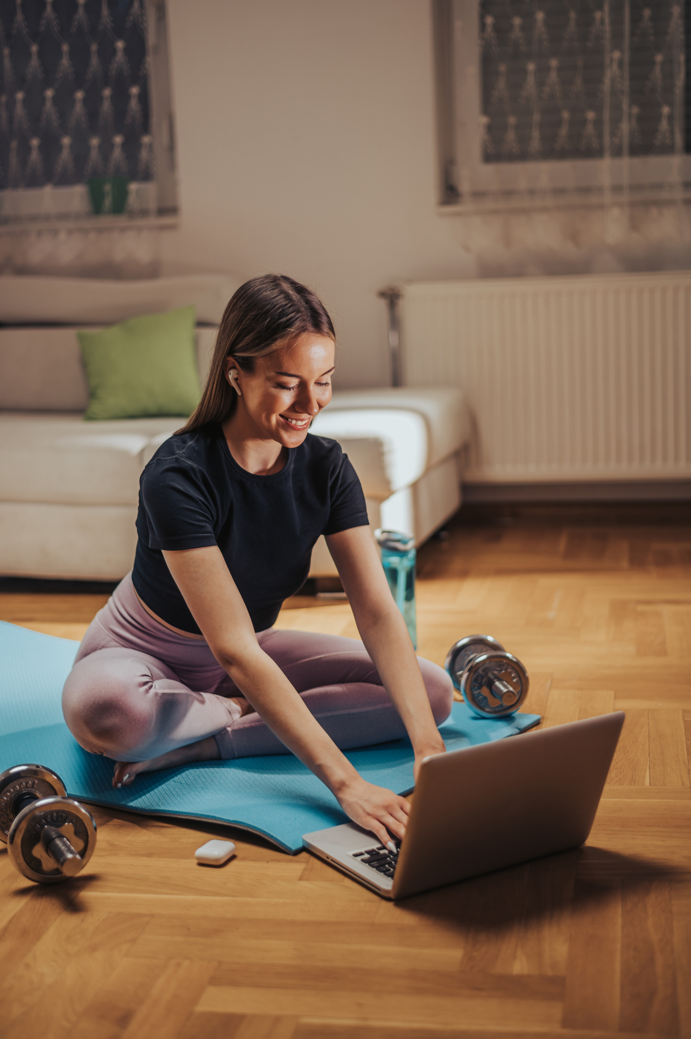 Young woman using laptop for an online instructions while training at home and sitting on a fitness mat