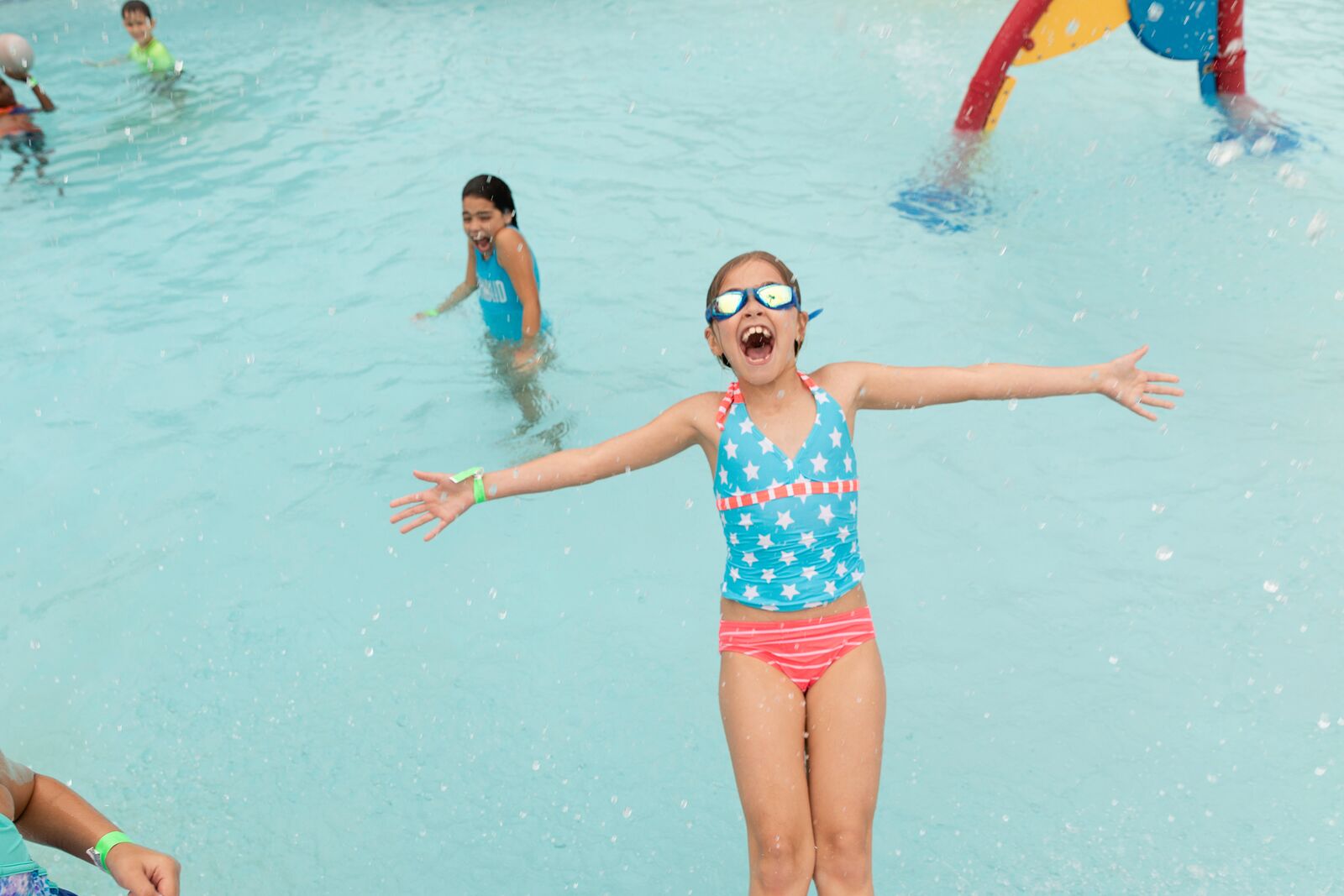 Girl falling backwards in pool with her arms wide open, smiling