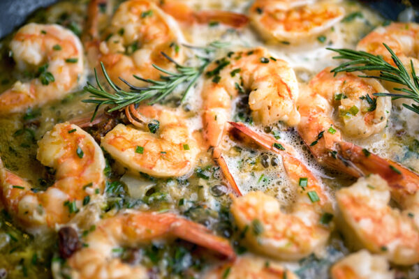 Close image of jumbo shrimp being sauteed in a pan with oregano, chive, rosemary, garlic and paprica creating Shrimp Scampi