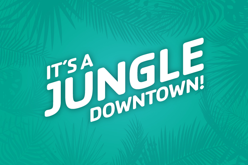 Image of green background with tropical foliage and the worlds It's a Jungle Downtown in white