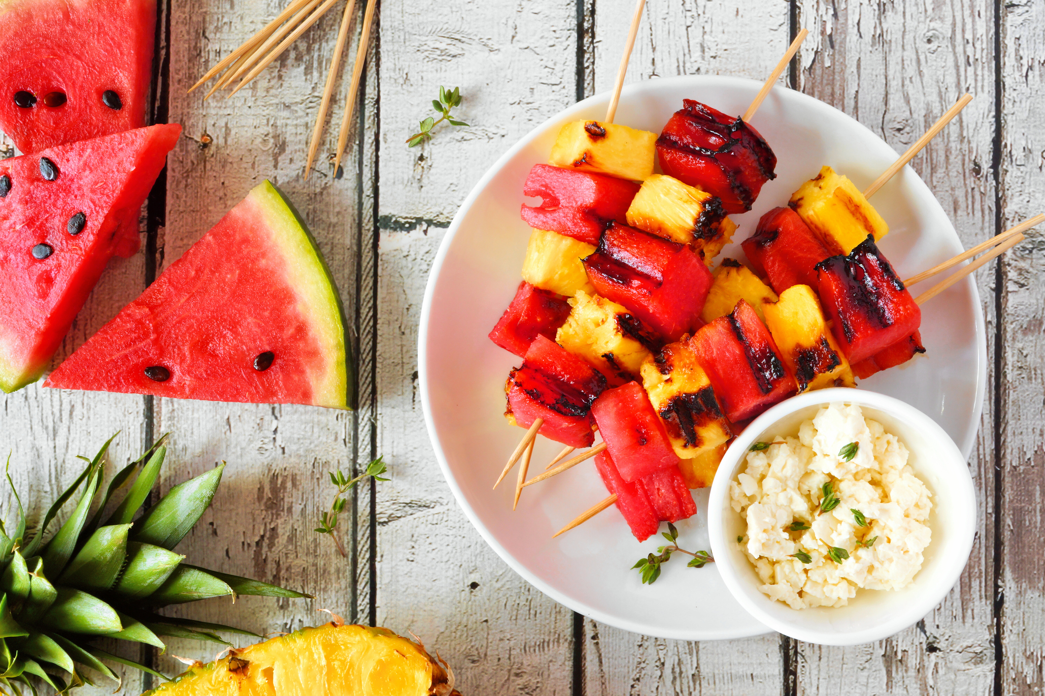 Grilled summer watermelon and pineapple fruit kabobs with feta, top view over white wood
