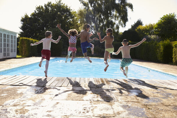 Rear View Of Children Jumping Into Outdoor Swimming Pool