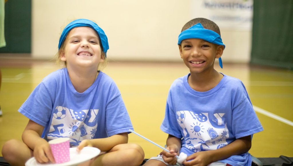 Young girl and boy smiling while eating together in the gym