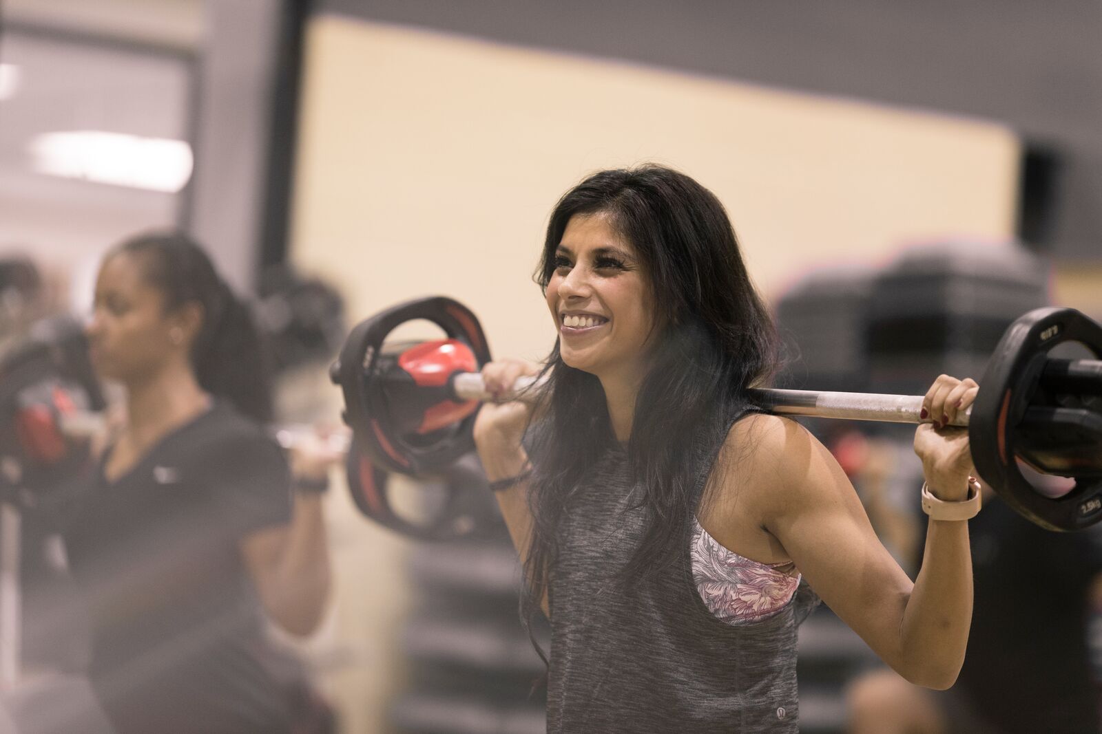 Woman taking BodyPump class at YMCA holding a barbell and smiling