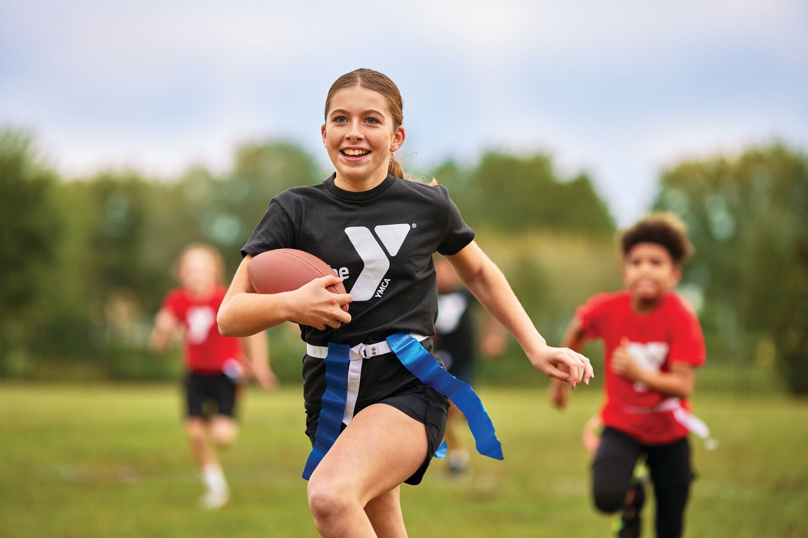 Girl running with football in flag football game while wearing a YMCA uniform