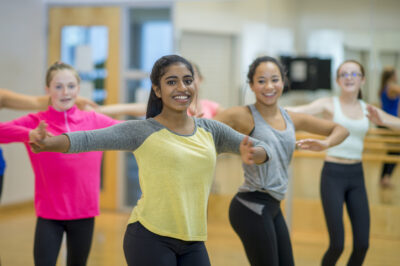 A multi-ethnic group of teenage girls are taking a dance class together at the gym.