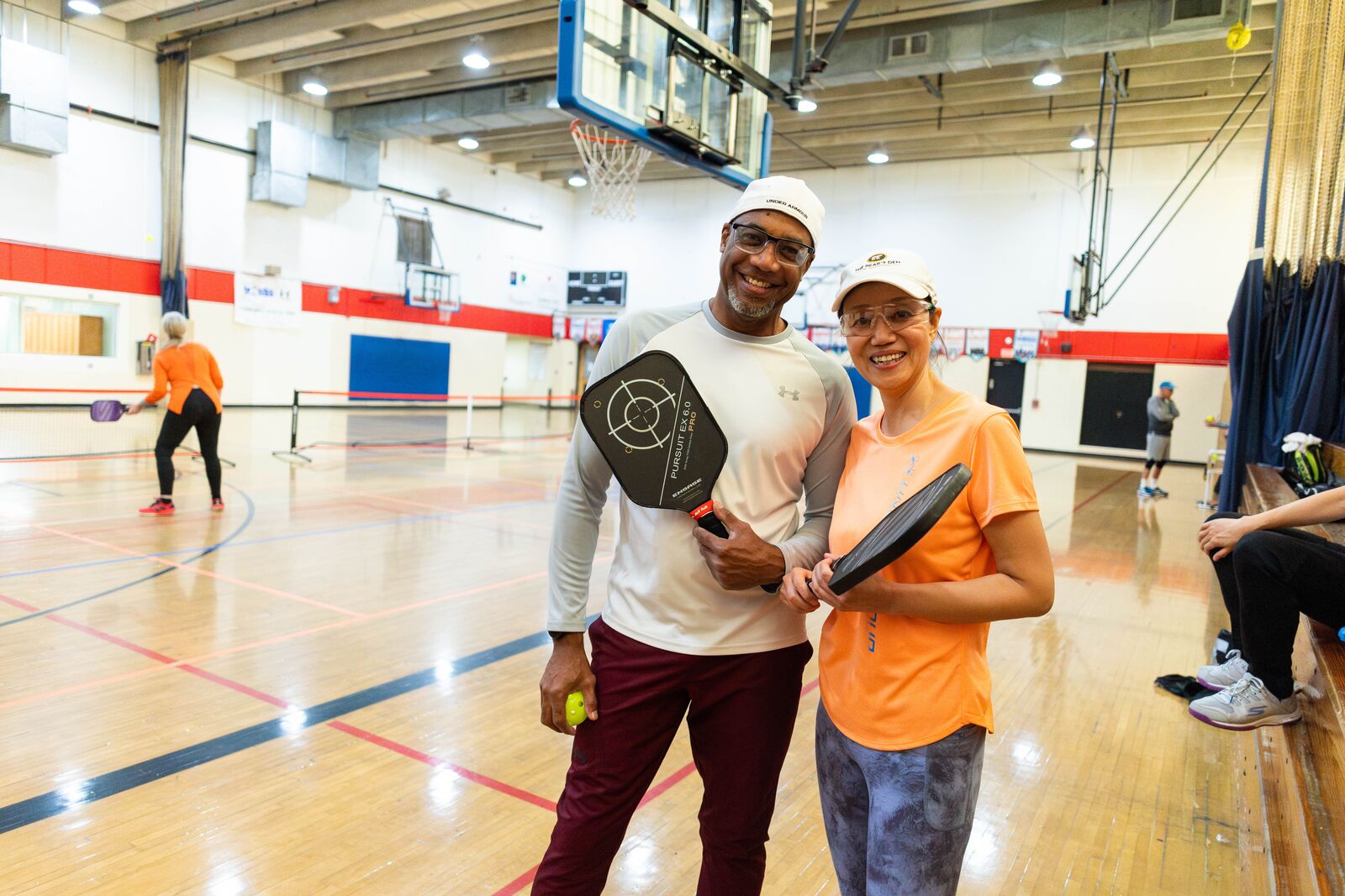 Two YMCA members smiling at the camera while holding pickleball paddles.