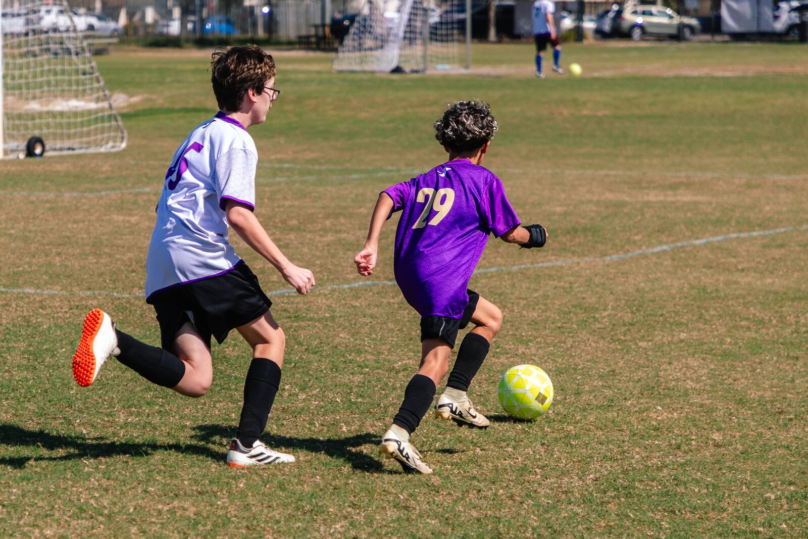Two teen kids running on a YMCA soccer field, facing away from the camera.