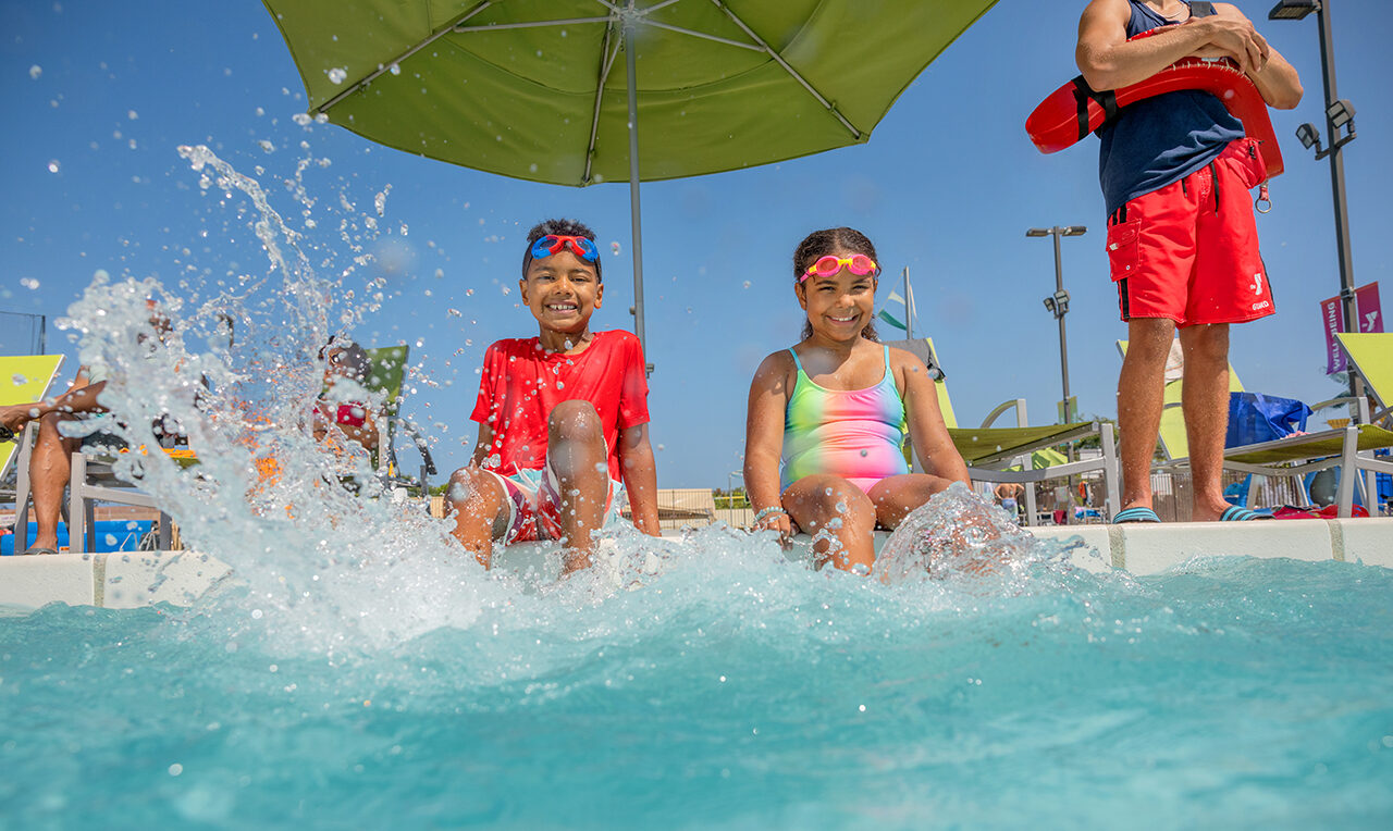 A boy and girl splashing their feet at the edge of the pool at the YMCA