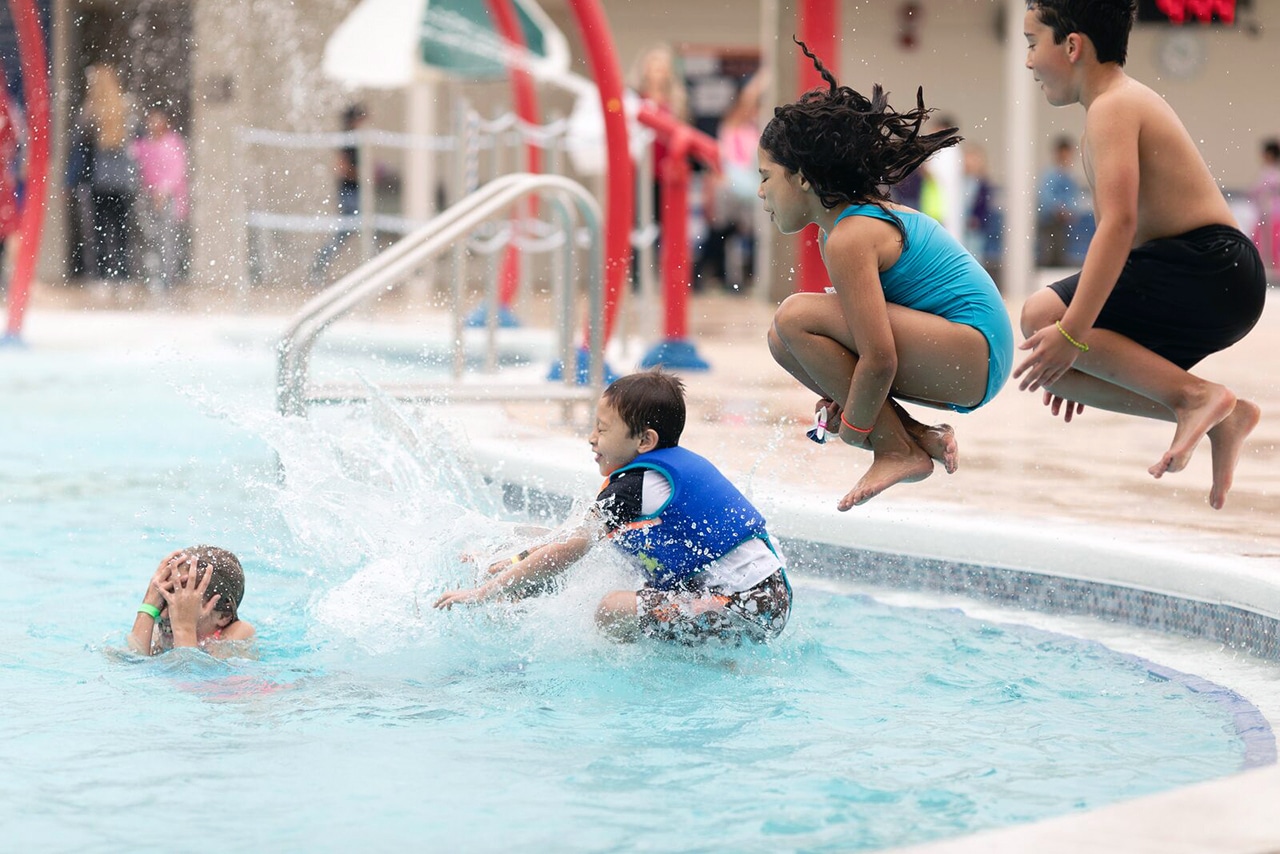 Kids jumping into a pool at the YMCA doing cannonballs in mid-air