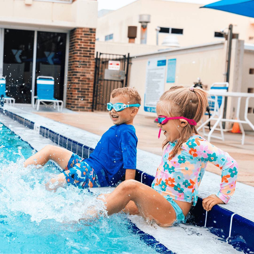 Two children splashing and playing at the poolside of a YMCA facility