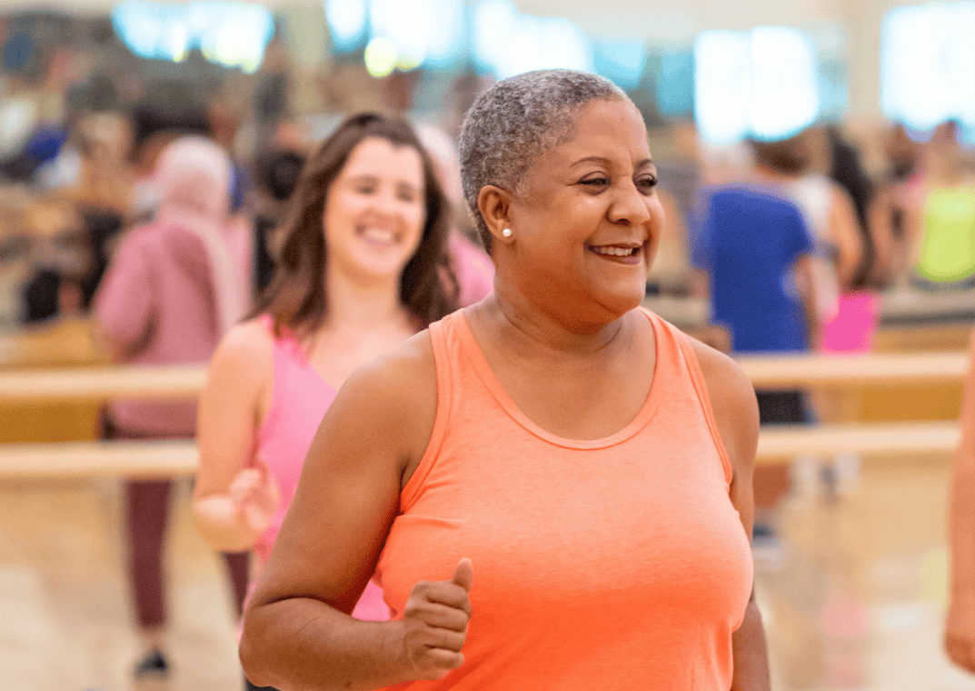 Two women participating in a group exercise class at the YMCA, smiling and moving to the workout.