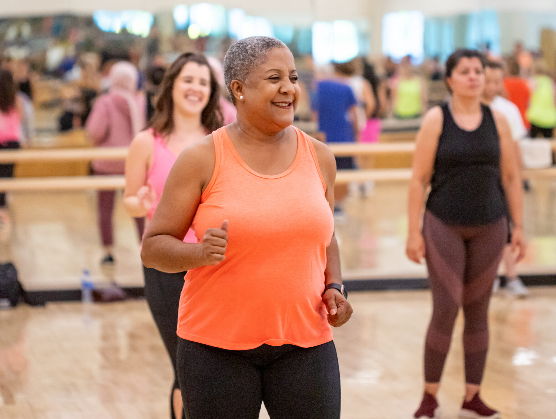Two people participating in a group exercise class at the YMCA, smiling and moving together.