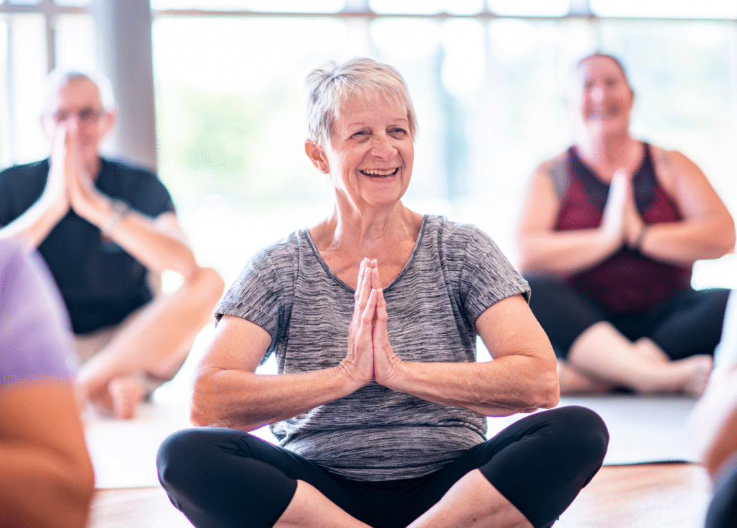 Three people practicing yoga together in a YMCA studio, stretching on mats and focusing on their poses.