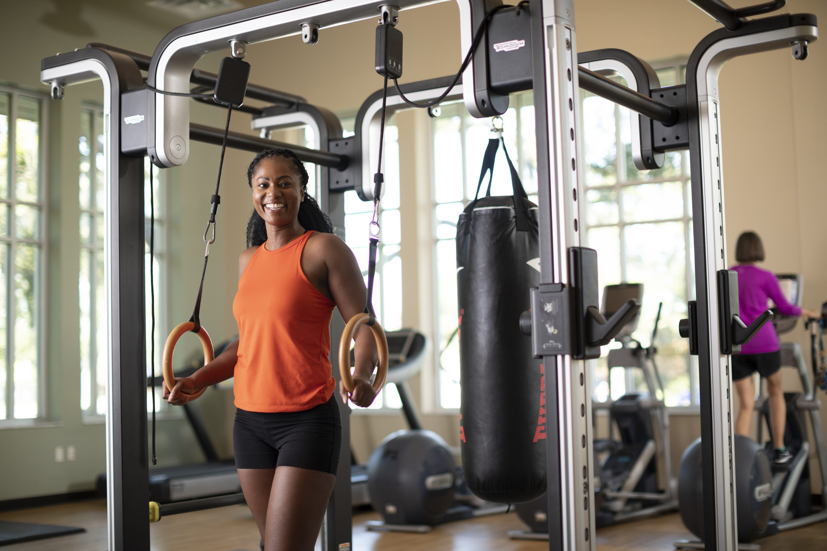 Woman working out on cardio equipment at the Y, surrounded by weights and fitness machines, with full access to pools, saunas, splash pads, and sports courts.