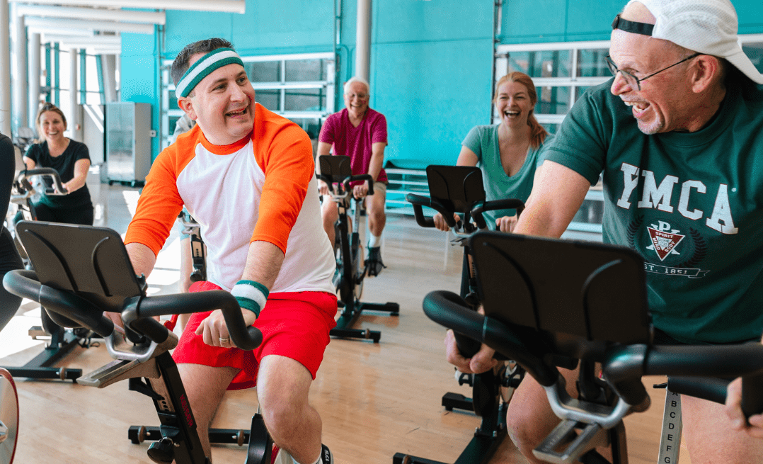 Two men cycling on stationary bikes at the YMCA, participating in an indoor cardio workout