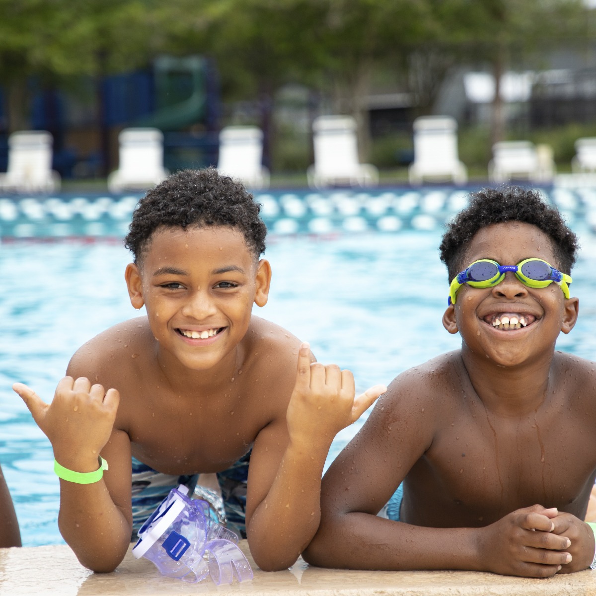 Two boys smiling and playing in a pool at the YMCA, representing youth development and water activities.